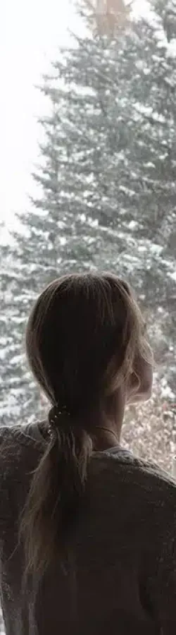 Donna osserva la neve da una finestra in alluminio con isolamento termico – comfort e protezione con Aluminia
