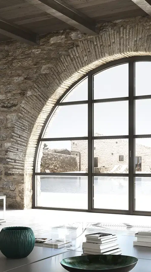 Finestra ad arco in alluminio minimal Aluminia in ambiente rustico moderno con vista su corte in pietra